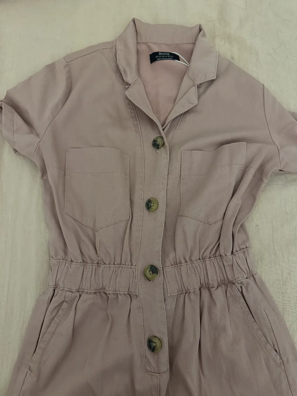 Mono largo de Bershka en color rosa viejo, con cuello camisero y botones. Posee bolsillos delanteros y cintura elastizada. Ideal para un look casual y cómodo. Muy buena calidad 60% Lyocell 40% Algodón. 