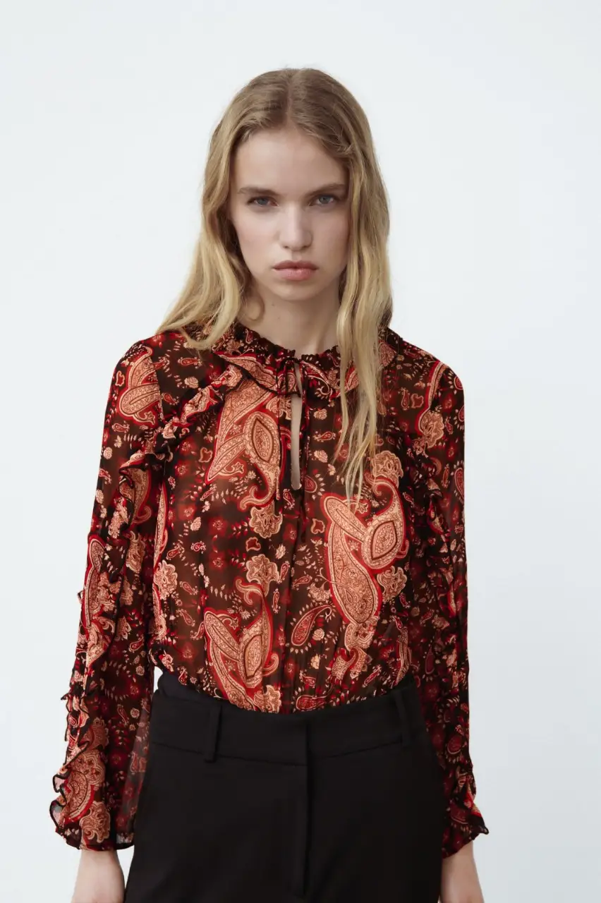 Body de mujer con estampado de paisley en tonos marrones y rojos. Cuello con lazo y mangas largas con volados. Ideal para un look elegante y sofisticado.
