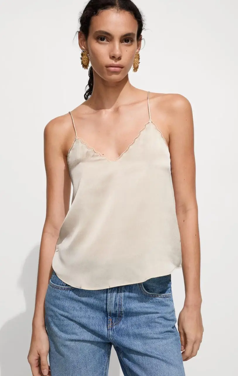 Top de satén color crudo con escote en pico y detalle de encaje. Diseño recto y tirantes finos. Ideal para un look elegante y fresco.