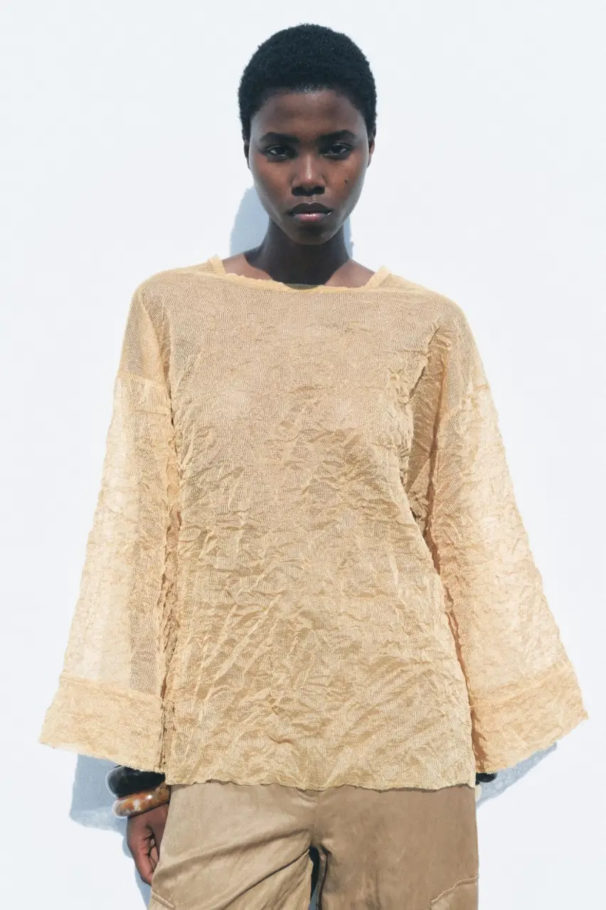 Blusa de cuello redondo y manga tipo kimono, con detalle de tejido arrugado. Cierre en espalda con aberturas y lazos. Ideal para un look casual y cómodo.