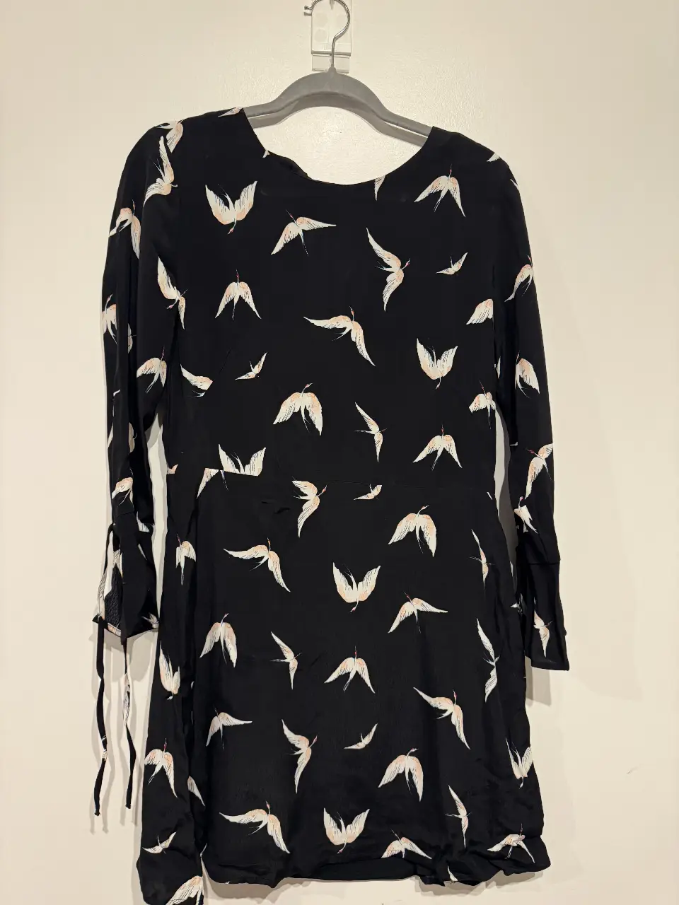 Vestido mini negro con estampado de pájaros blancos y detalles en rosa. Mangas largas con lazos en los puños y escote en la espalda.