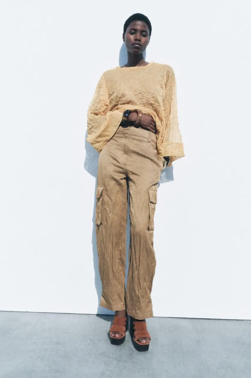Pantalón cargo de hilatura con algodón, tiro medio y cintura con trabillas. Bolsillos de plastrón con solapa en pierna. Detalle de tejido arrugado. Cierre frontal con cremallera, botón y gancho metálico.