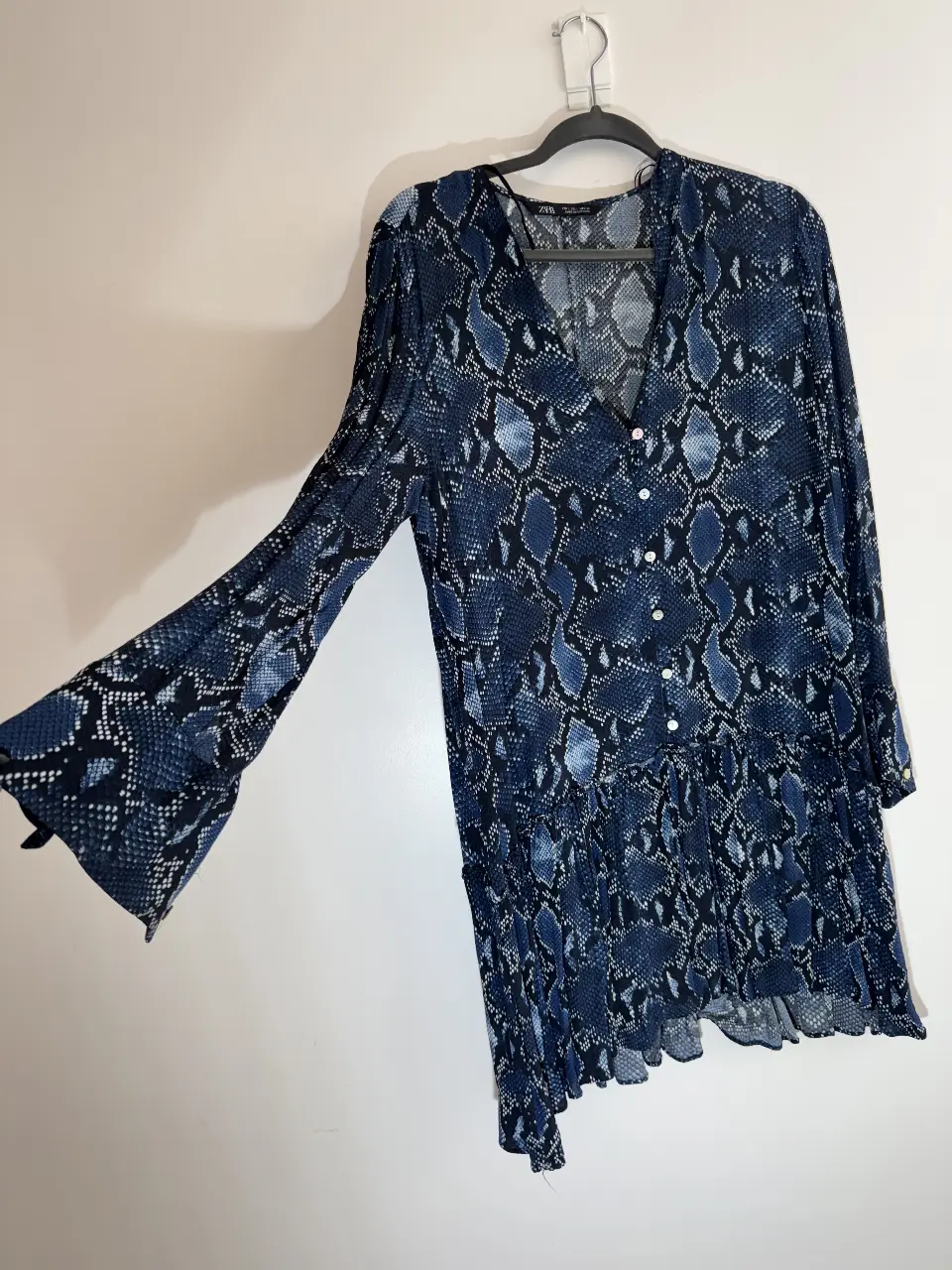 Vestido midi con estampado de serpiente en tonos azules y blancos. Diseño con mangas largas acampanadas, botones delanteros y detalle de volantes en la falda. Ideal para un look moderno y sofisticado.