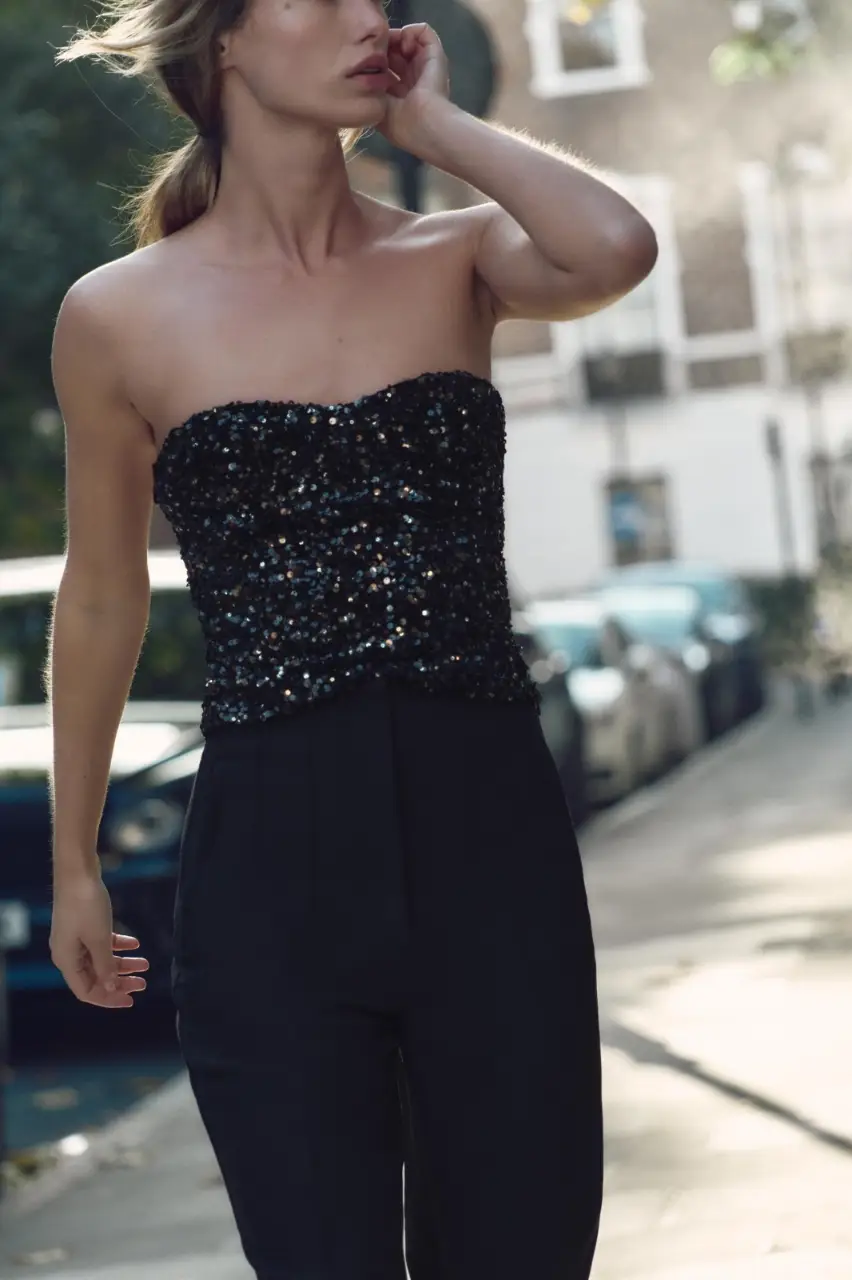 Top corto de fiesta con lentejuelas negras. Diseño strapless con escote recto y cierre lateral con cremallera oculta. Ideal para eventos y salidas nocturnas.