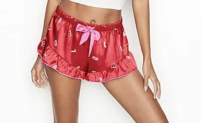Short de pijama de satén rojo con volados y lazos rosas. Estampado con letras blancas. Ideal para estar cómoda y fresca en casa.