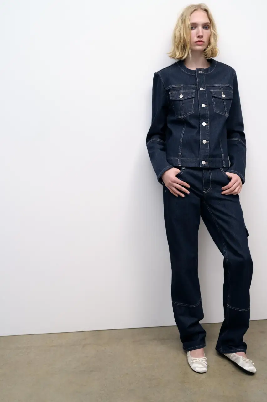 Conjunto de jean azul oscuro, compuesto por una chaqueta con cuello redondo y cierre con botones, y un pantalón recto con un bolsillo lateral. Ideal para un look casual y moderno.