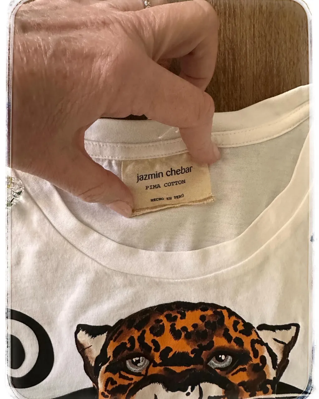 Remera blanca con estampa de dos leopardos rugiendo y un diseño abstracto en el centro. Posee detalles de rayas rojas y azules en la parte inferior.