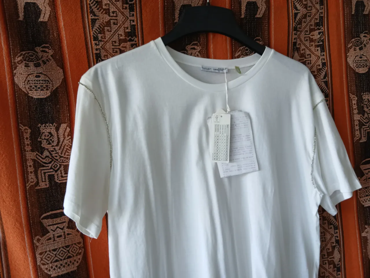 Remera blanca de algodón con detalles de strass en los hombros y mangas. Un toque de brillo para elevar tu look casual.