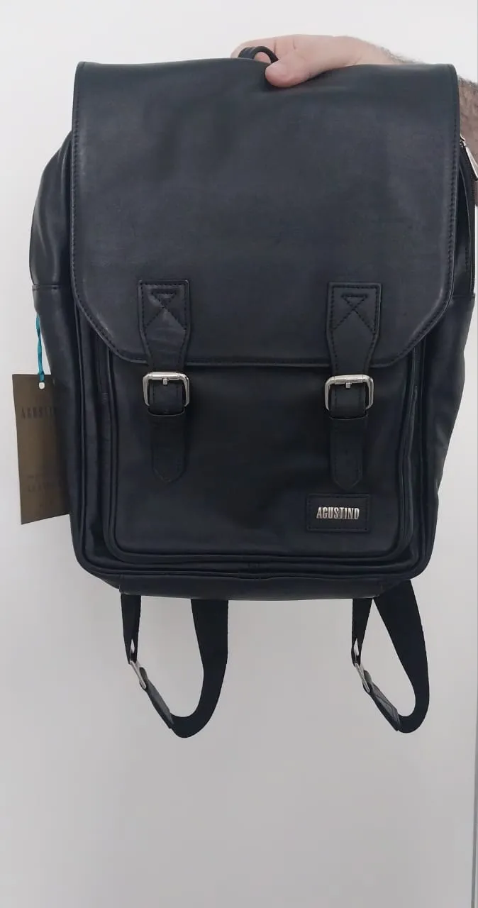 Mochila de cuero negra con dos hebillas en el frente y un bolsillo con cierre. Tiene dos tiras para llevar en la espalda. Incluye etiqueta de marca.