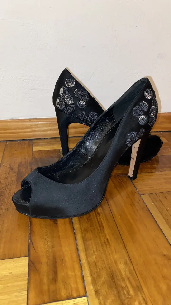 Elegantes zapatos de taco alto negros con detalles de flores en la parte trasera. Ideales para eventos formales y fiestas. Marca Las Oreiro