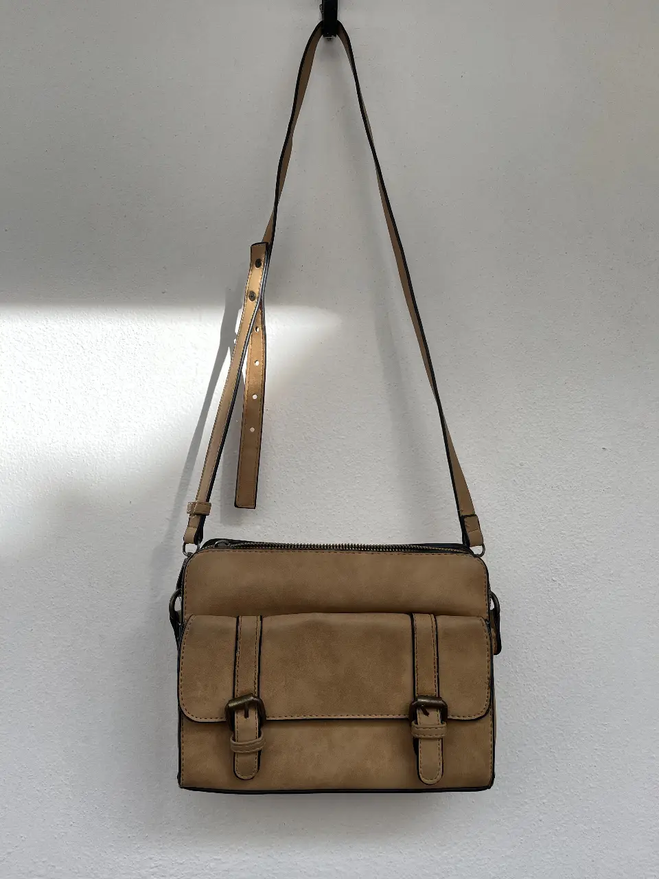 Cartera bandolera de gamuza sintética en tono marrón. Cuenta con dos bolsillos frontales con hebillas y un compartimento principal con cierre. Está en perfecto estado pero hay que cambiarle el cierre.