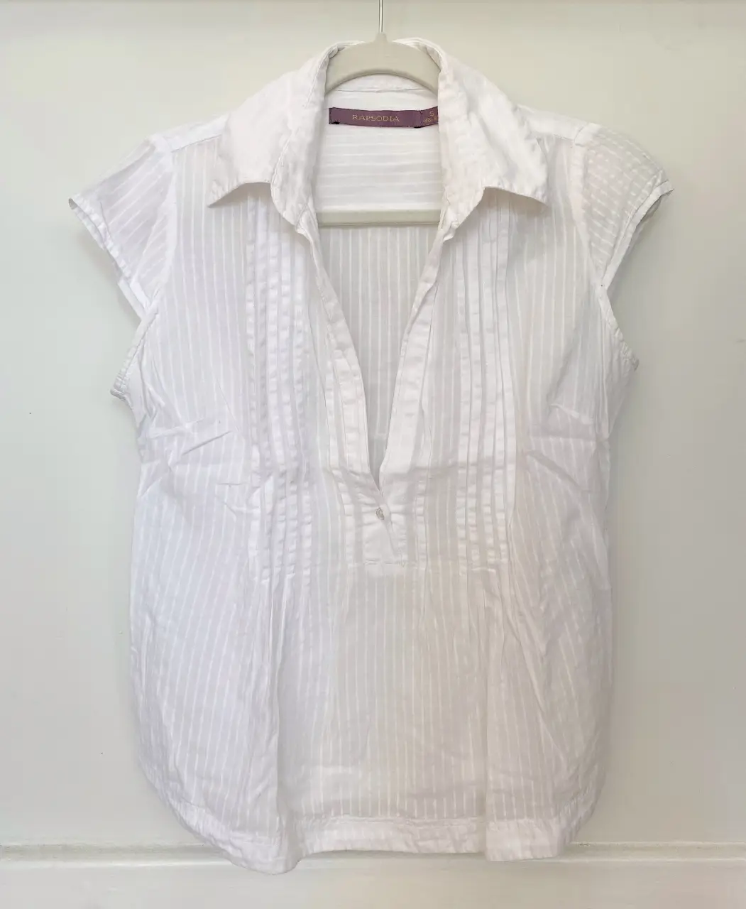 Blusa blanca tipo musculosa con cuello camisero y detalle de alforzas en el frente. Marca: Rapsodia.