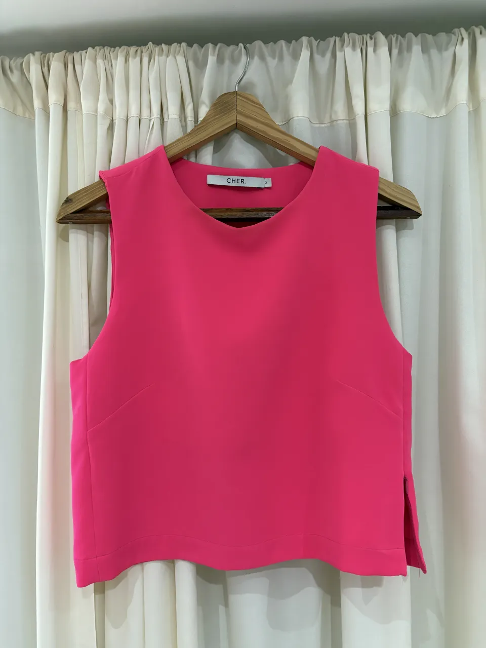 Top rosa fucsia sin mangas, con escote redondo y tajos laterales. Ideal para un look moderno y canchero.