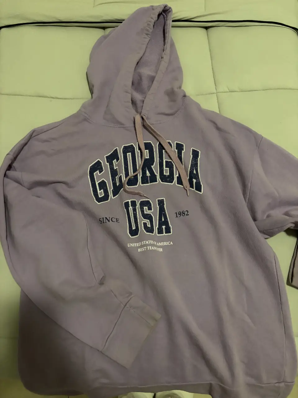 Buzo canguro de color violeta con estampado "GEORGIA USA 1982" en la parte delantera. 