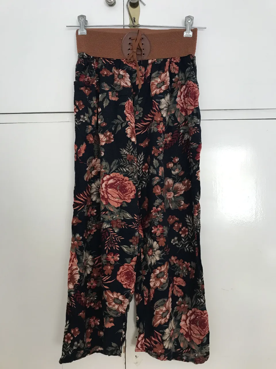 Pantalón suelto de mujer con estampado floral en tonos rojos y azul oscuro. Cintura con detalle de cinturón marrón con cordones. Ideal para un look casual y cómodo.
