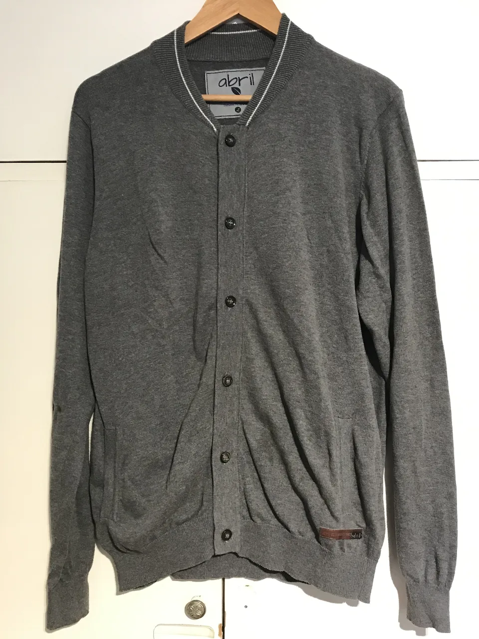 Cardigan gris de hombre, con cuello tipo polera y cierre con botones. Detalles en blanco en el cuello y puños. Ideal para un look casual y abrigado.