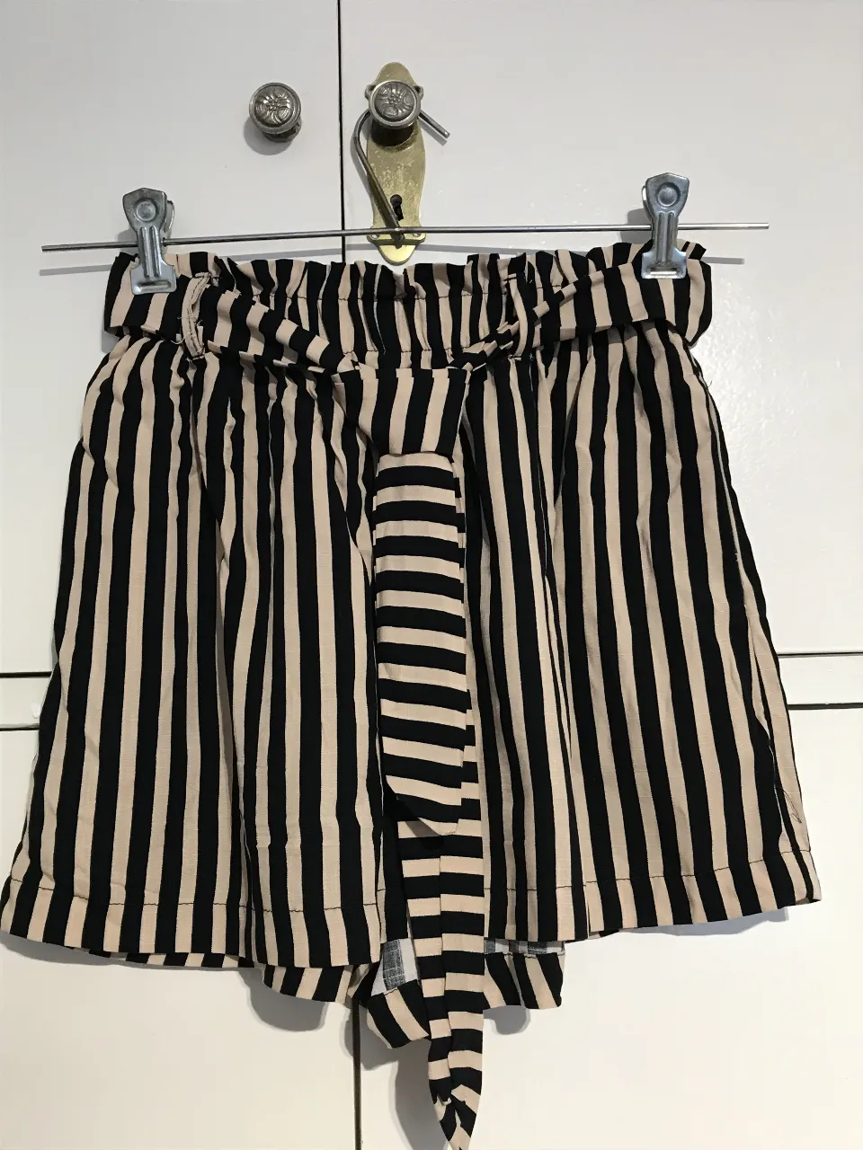 Shorts de tiro alto a rayas verticales en beige y negro. Con cintura elastizada y lazo para ajustar. Ideal para un look casual y fresco.