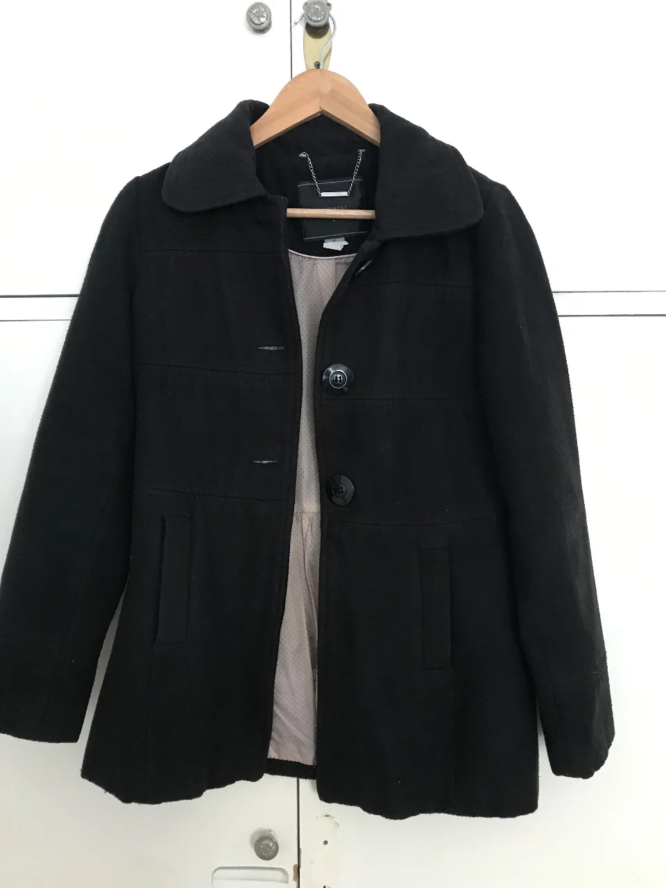 Tapado negro de paño, con cuello solapa, dos bolsillos frontales y cierre con botones. Interior forrado con tela estampada.