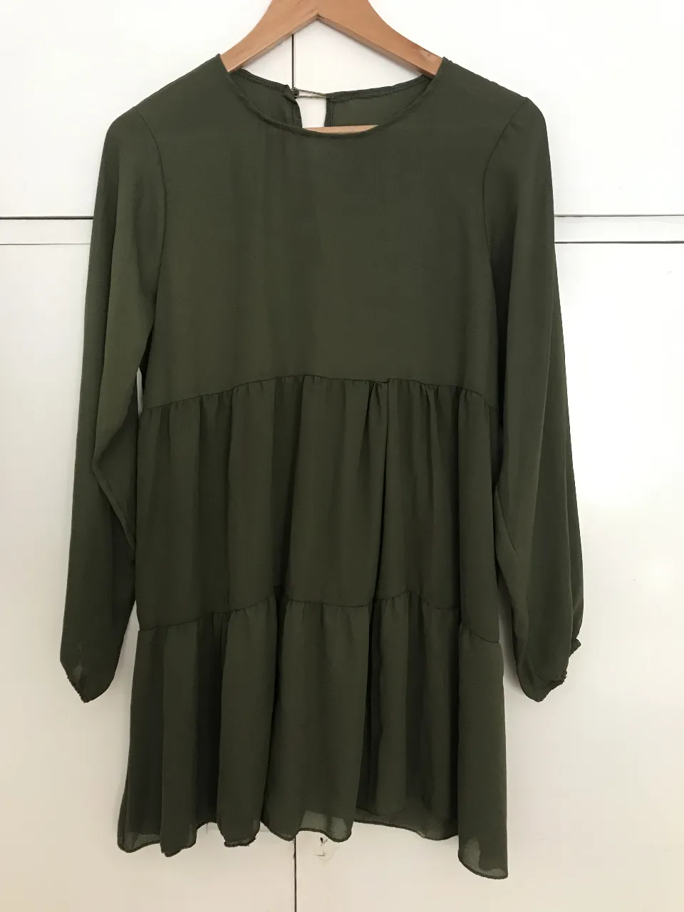 Vestido corto de manga larga con elástico en color verde oscuro, con diseño de volados y detalle de botón en la espalda. Ideal para un look casual y cómodo.