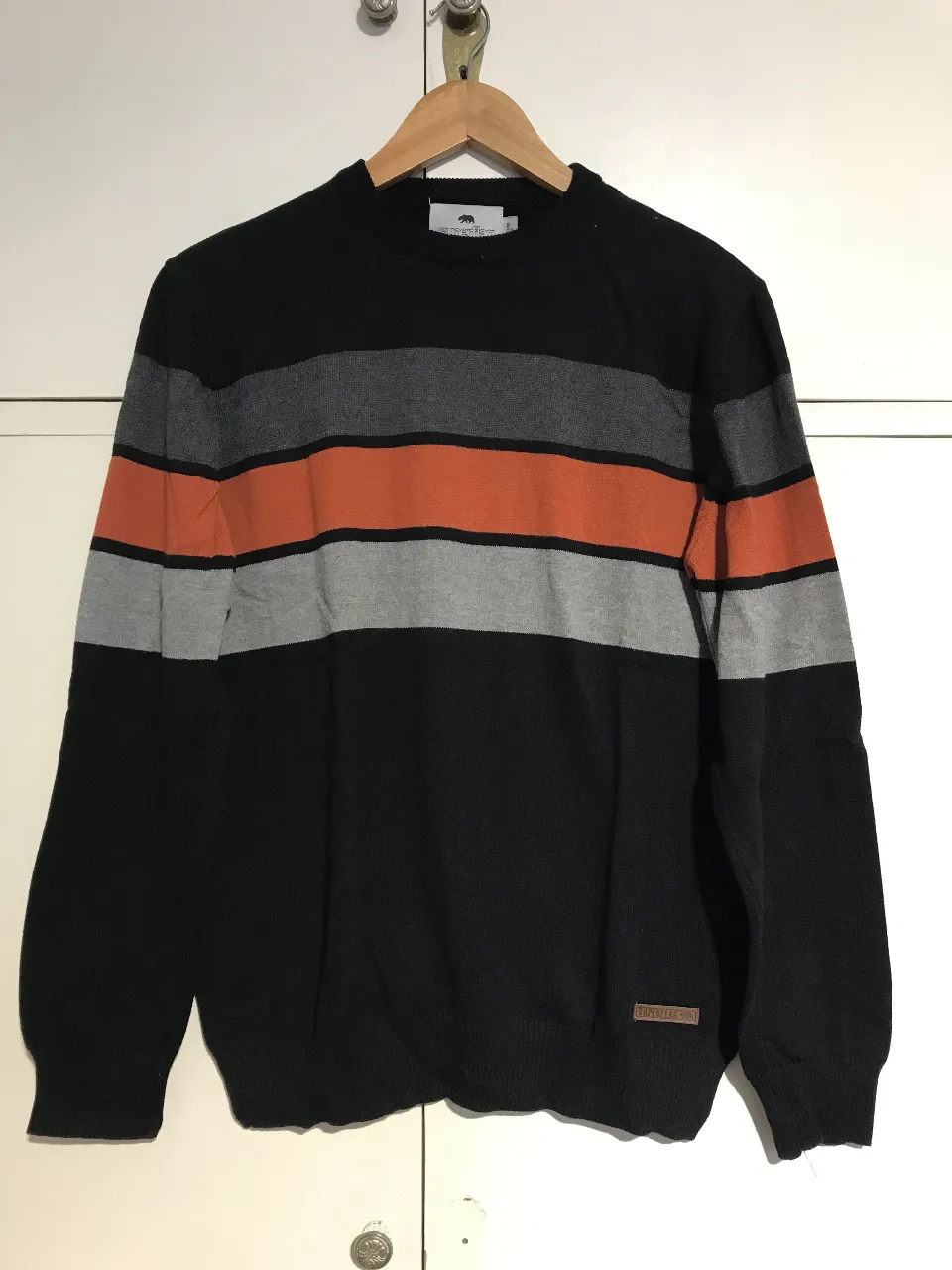 Sweater de hombre a rayas horizontales en color negro, gris y naranja. Cuello redondo. Marca Superflag.