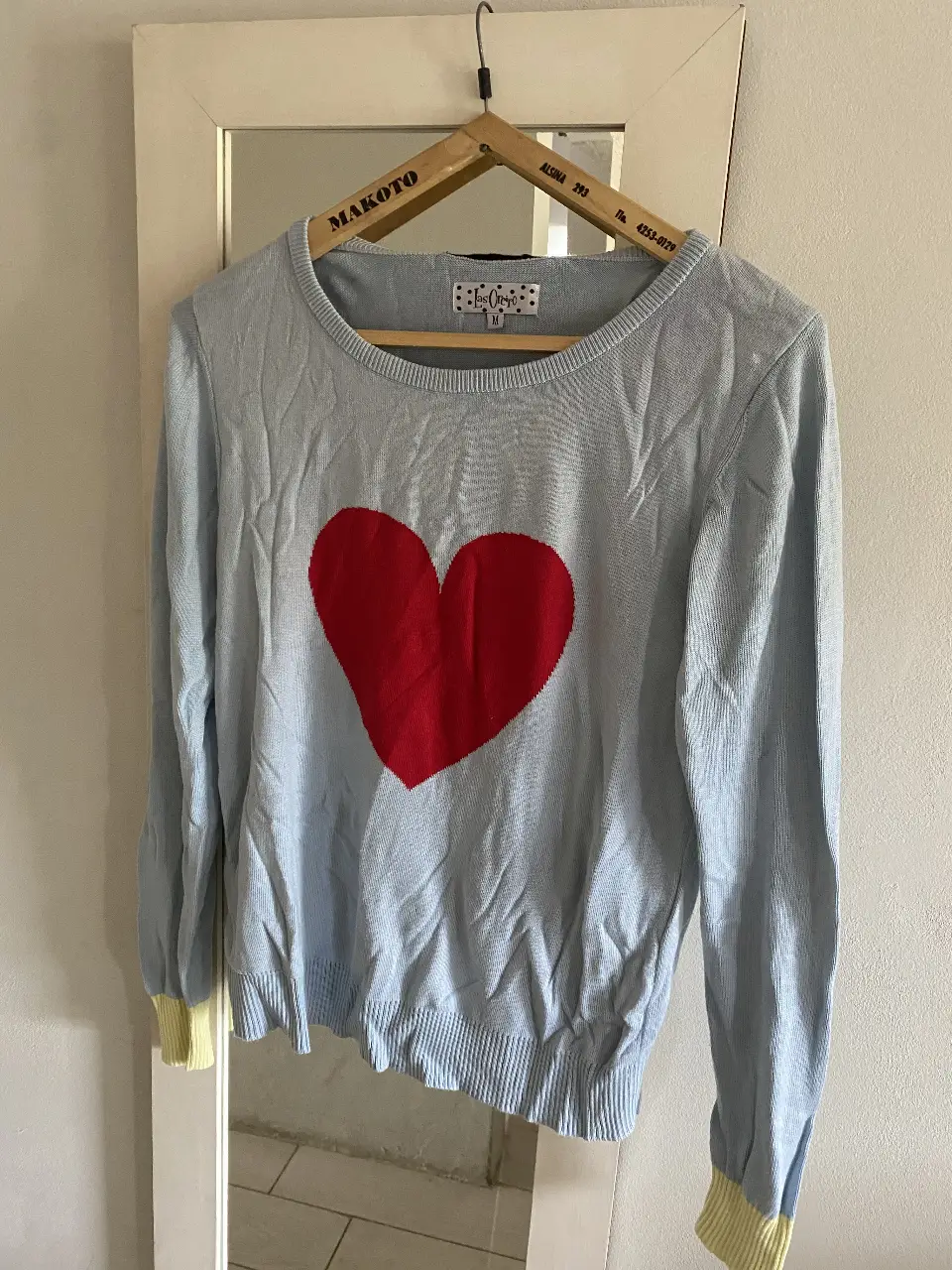 Sweater de mujer celeste con un corazón rojo en el centro. Tiene detalles en amarillo en los puños. En la espalda tiene un moño negro. Talle M.
