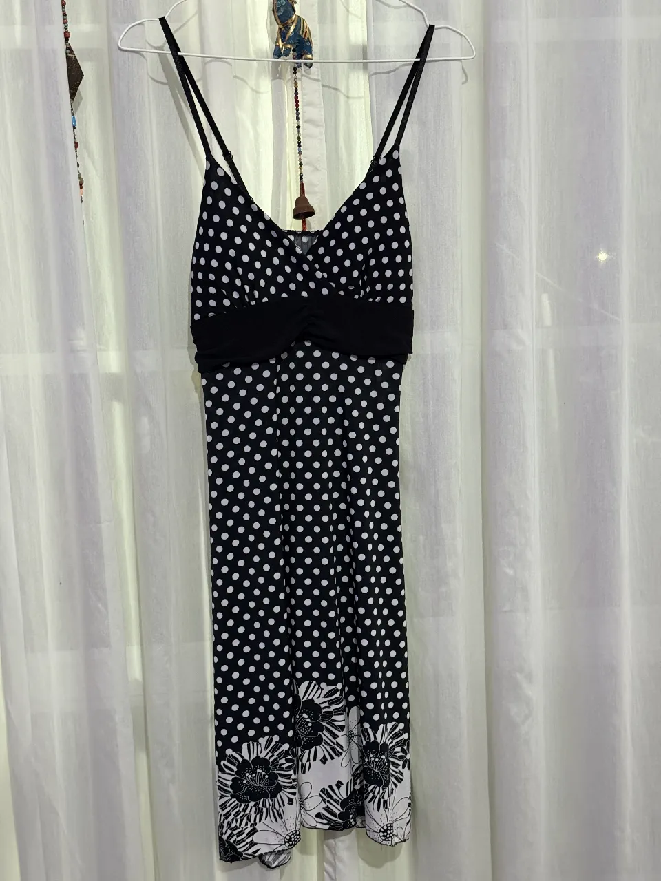 Vestido corto de mujer con estampado de lunares blancos sobre fondo negro. Tiene un detalle fruncido en la cintura y tirantes finos. Ideal para una salida casual o una fiesta.