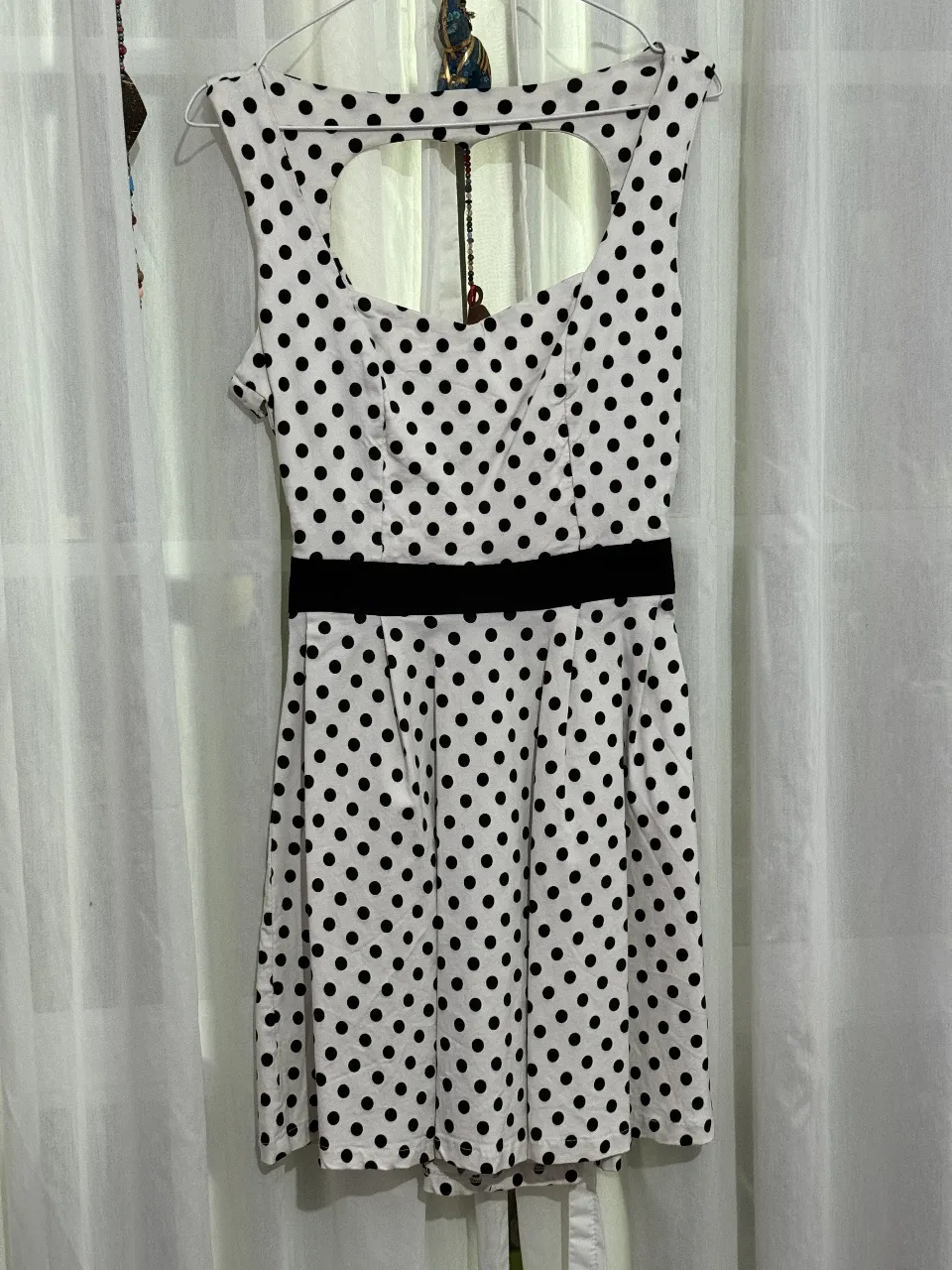 Vestido mini de mujer con estampado de lunares en blanco y negro. Diseño con escote en la espalda y detalle de cinturón negro en la cintura. Ideal para un look retro y femenino.