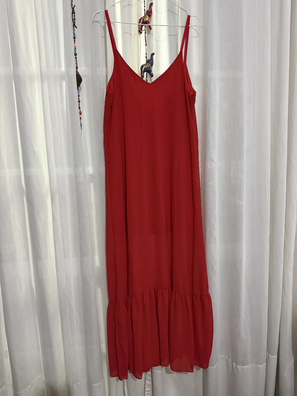 Vestido midi rojo con tirantes finos y escote en V. Diseño liso con volados en el ruedo, ideal para un look fresco y femenino.