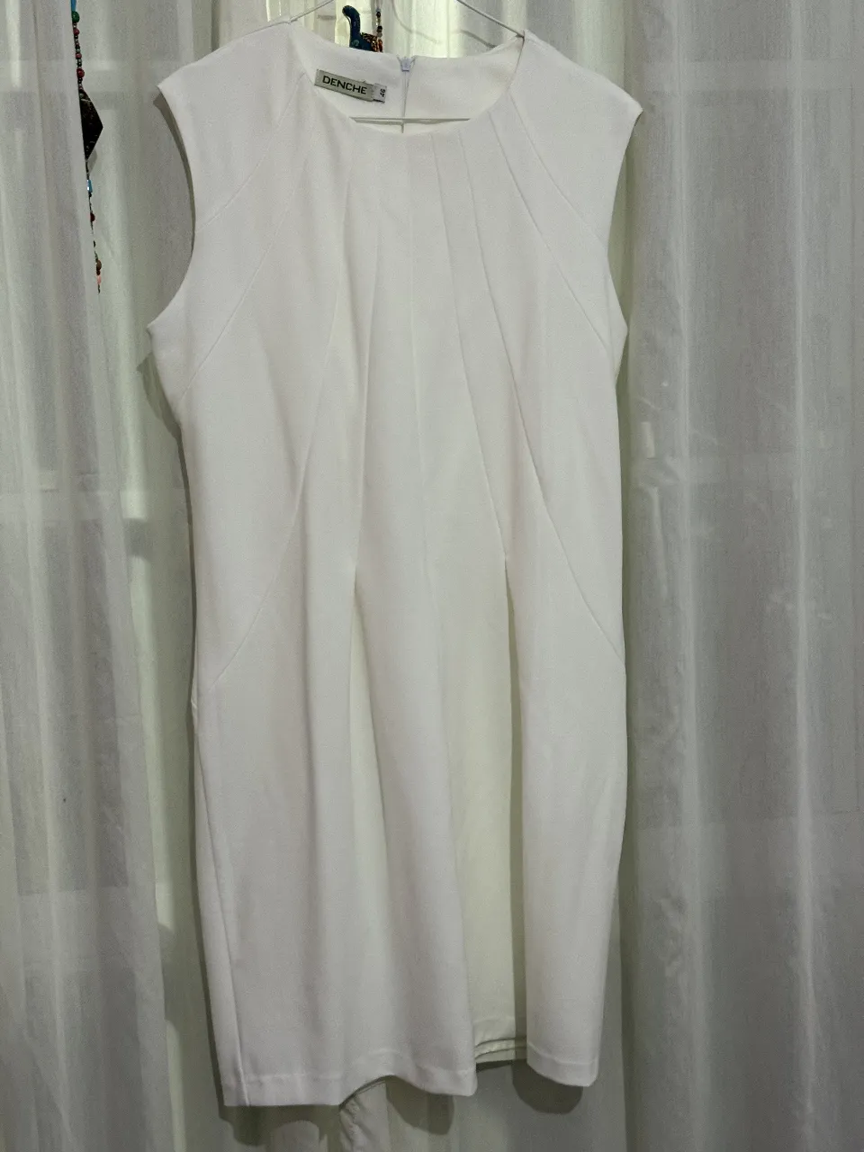 Vestido midi blanco de la marca Denche, con diseño elegante y detalles plisados en la parte delantera. Ideal para ocasiones formales o eventos especiales. Corte recto y sin mangas.
