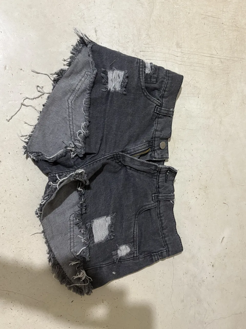 Shorts de jean tiro bajo, con roturas y detalles desflecados en los bordes. Diseño de patchwork en los laterales y parches de rotura en el frente. Ideales para un look canchero y moderno.