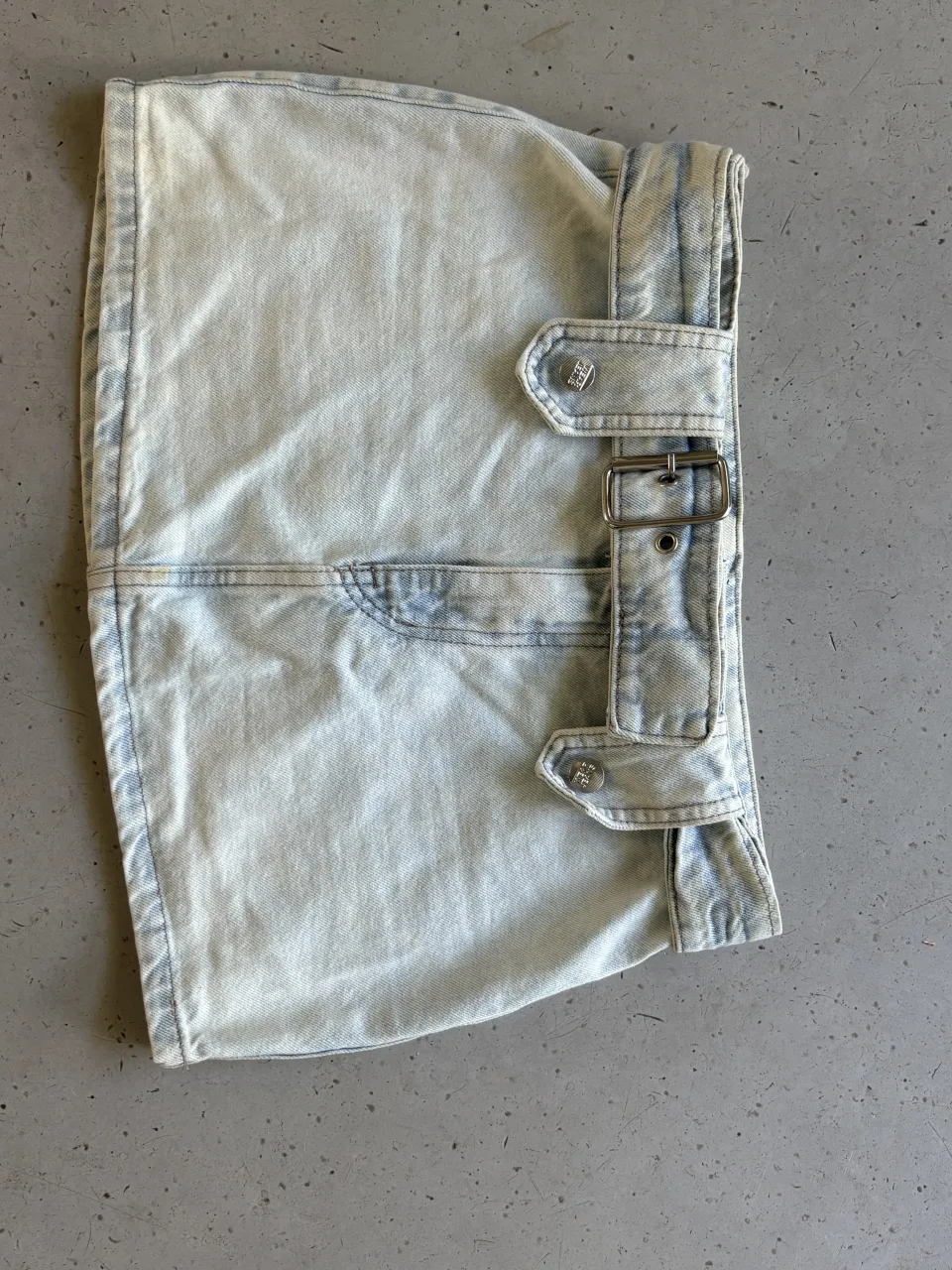 Pollera de jean tiro medio con tiradores y hebillas metálicas. Lavado desgastado y detalles de costuras. Estilo Y2k.