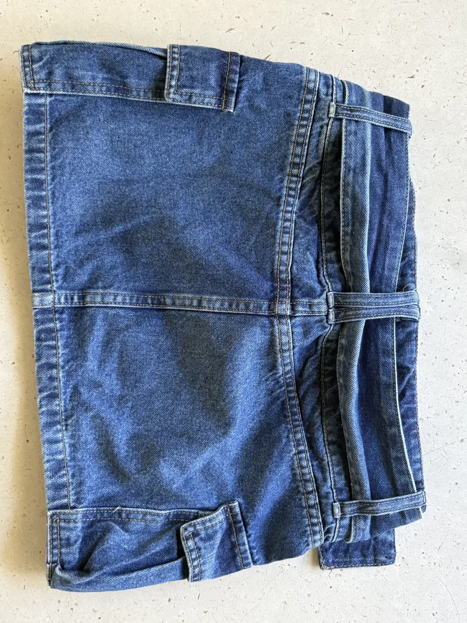 Pollera de jean tiro medio Y2k con cinturón de hebillas y tachas. Diseño cargo con bolsillos y detalles de costuras. Lavado clásico de denim.