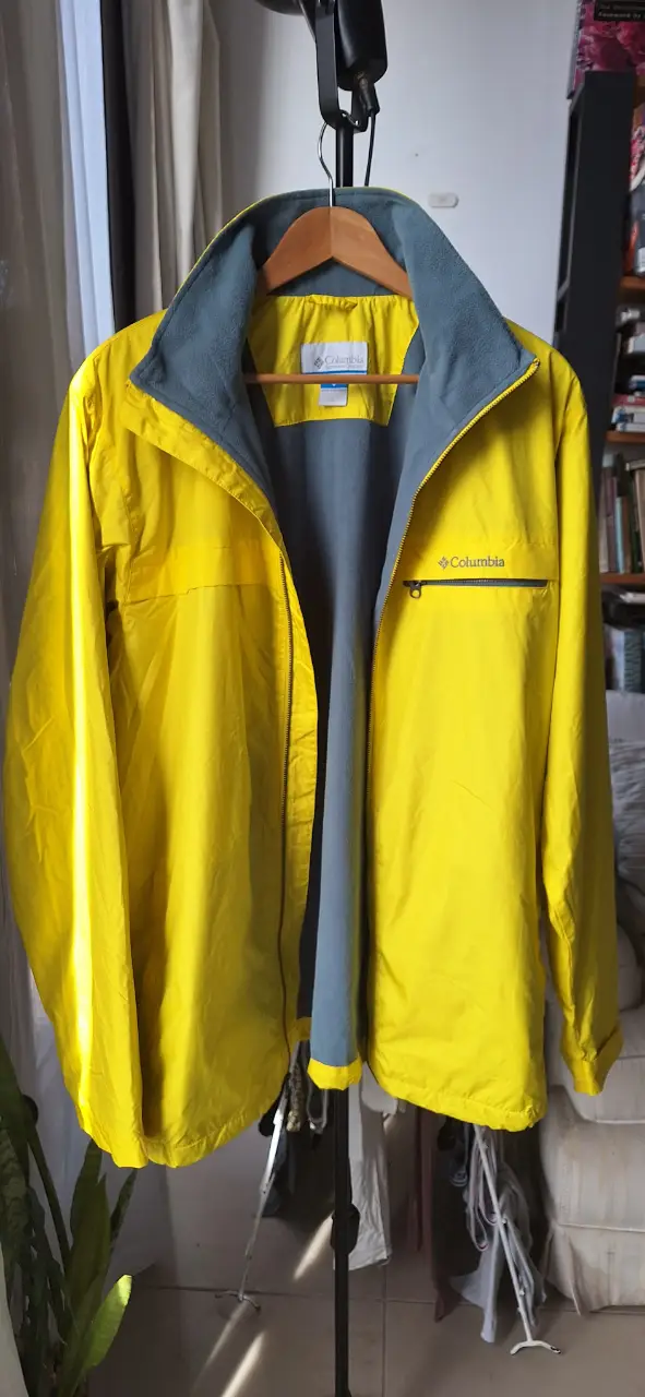 Campera rompevientos amarilla Columbia para hombre. Con cierre frontal, cuello alto con interior gris y bolsillo con cierre en el pecho. Ideal para actividades al aire libre.