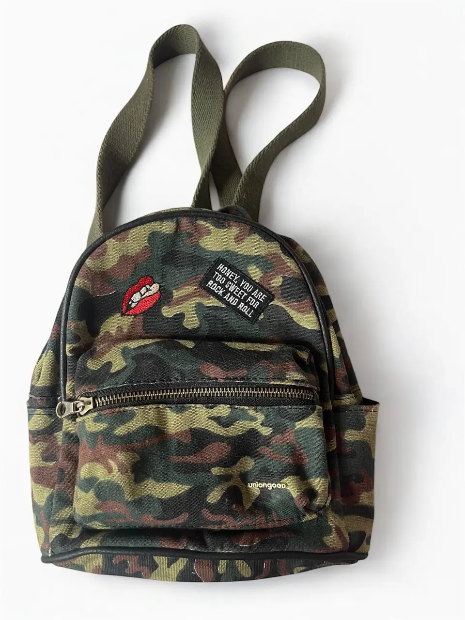 Mochila camuflada con parche de labios y frase. Ideal para un look urbano y canchero. Perfecta para llevar tus esenciales con estilo. 