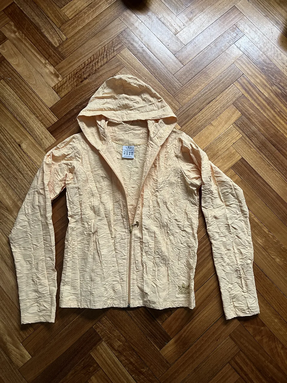 Buzo con cierre Adidas, color amarillo claro, con capucha y textura arrugada. Ideal para un look casual y deportivo.