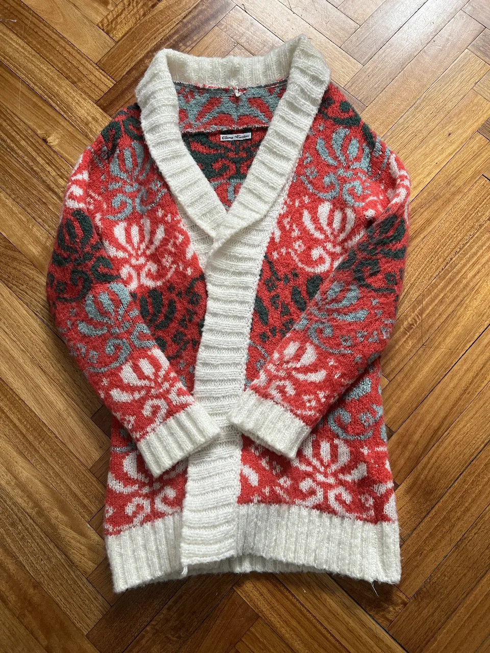 Cardigan de lana tejido con diseño floral en rojo, blanco, verde y gris. Cuello y puños en blanco. Ideal para un look vintage y abrigado.