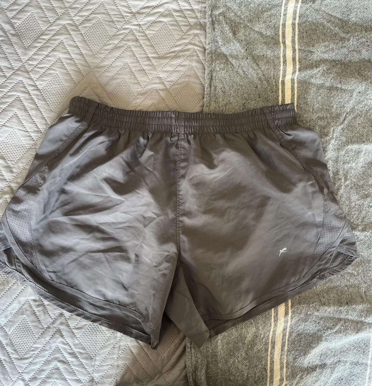 Short deportivo gris para mujer, ideal para running y entrenamiento. Confeccionado con tejido ligero y transpirable, cuenta con detalles perforados para mayor ventilación y un calce cómodo. Perfecto para tus rutinas de ejercicio.