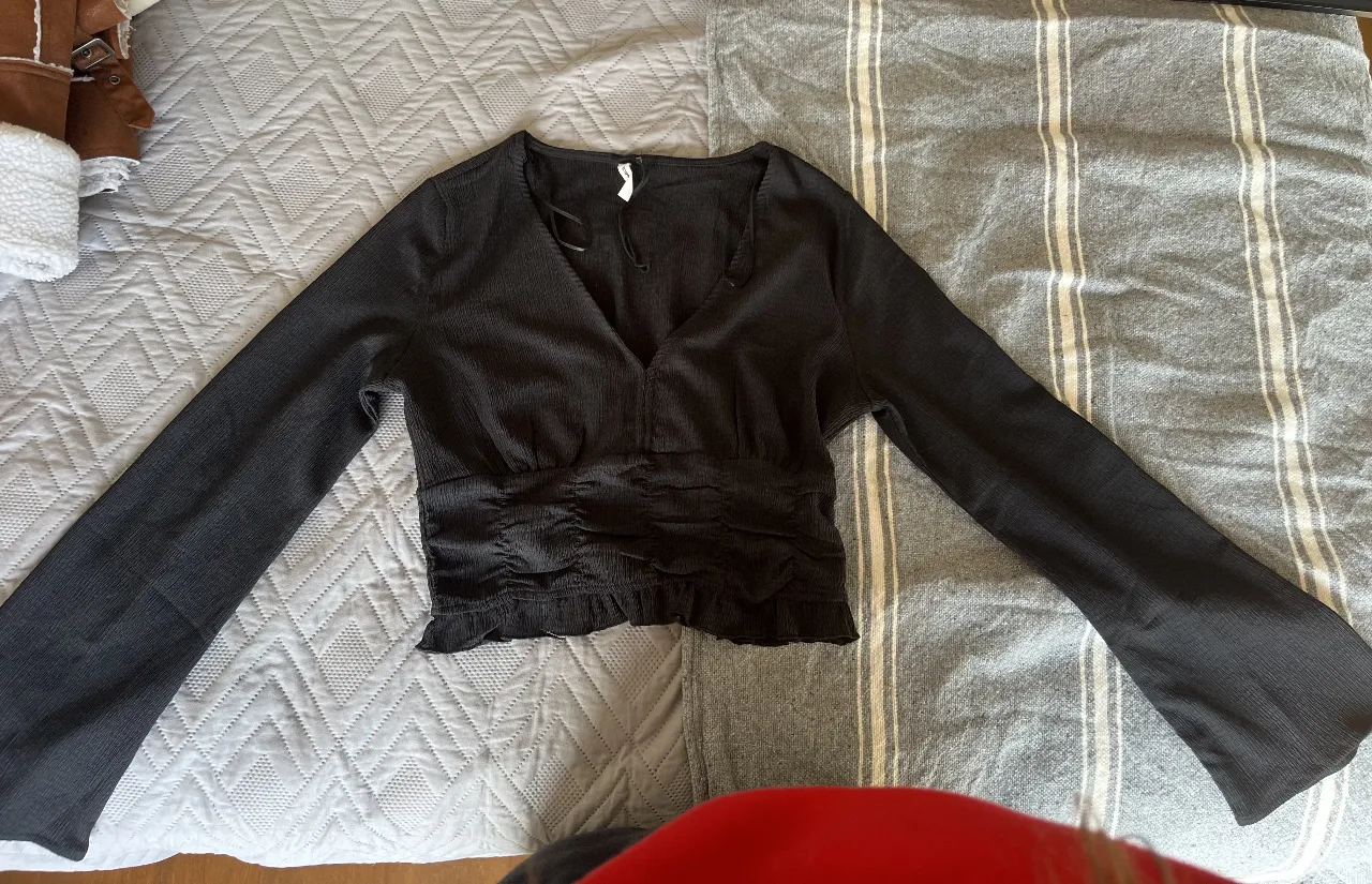 Blusa negra de manga larga con escote en V y detalle fruncido en la cintura. Ideal para un look elegante y versátil.