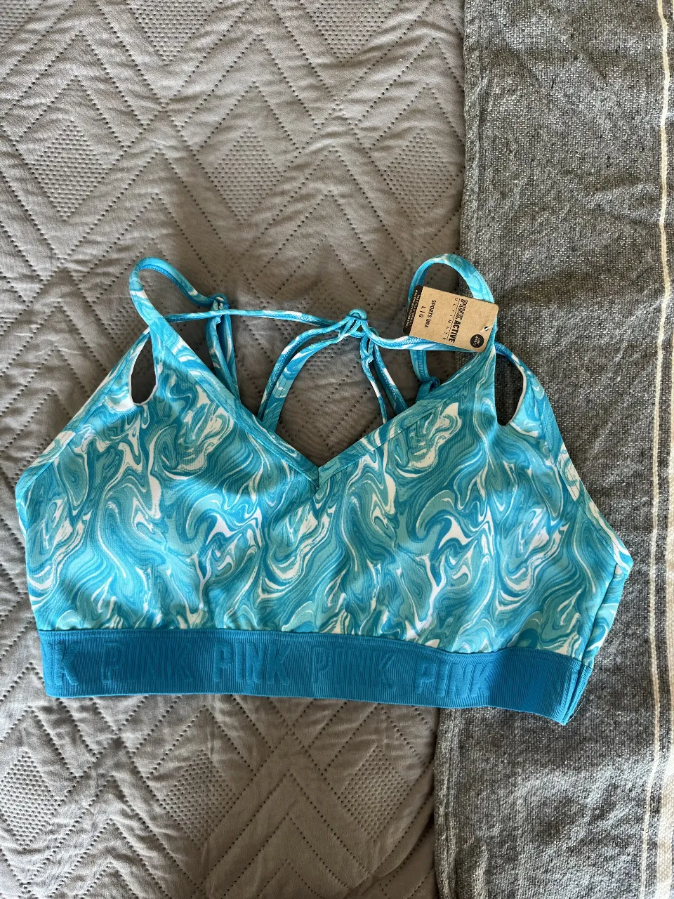 Top deportivo de mujer, con estampado de olas en tonos celeste y blanco. Tiene elástico en la base con la marca PINK. Ideal para actividades de bajo impacto.