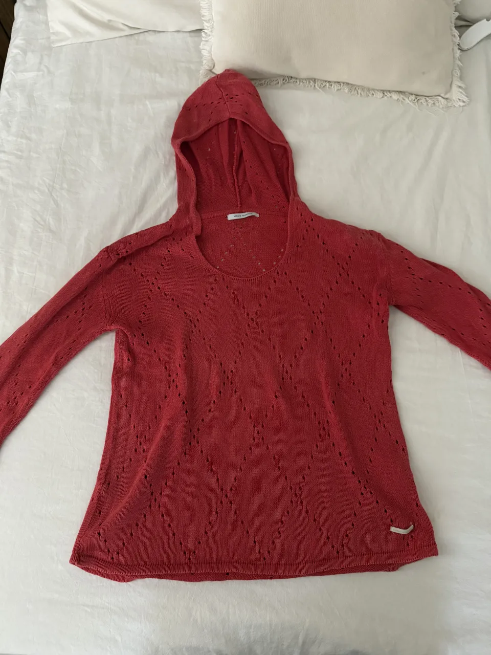 Sweater tejido con capucha, manga larga y detalles calados en forma de rombos. Color rojo vibrante, ideal para un look casual y canchero. Perfecto para los días frescos de entretiempo o para complementar un outfit de verano a la noche.