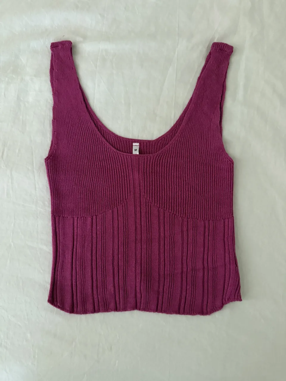 Musculosa tejida de morley color fucsia. Tiene un escote en V pronunciado y un corte que entalla en la cintura, luego se abre ligeramente. Ideal para un look casual o para usar en la playa.