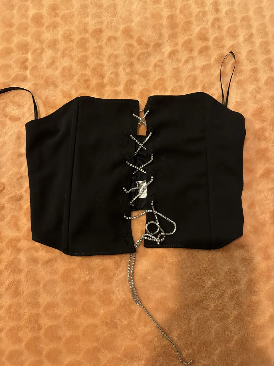 Top negro con tiras finas y escote en V. Posee cordones cruzados con strass en la parte delantera y una cadena de strass colgante.