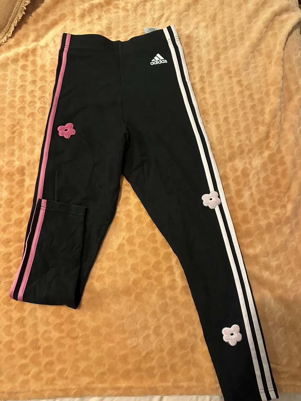 Calza negra deportiva Adidas con detalles de flores rosas y tres tiras blancas y rosas en los laterales.