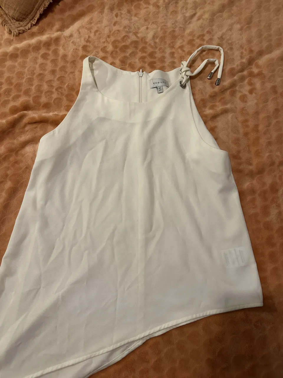 Musculosa blanca con detalle de tiras anudadas en el cuello y cierre en la espalda.