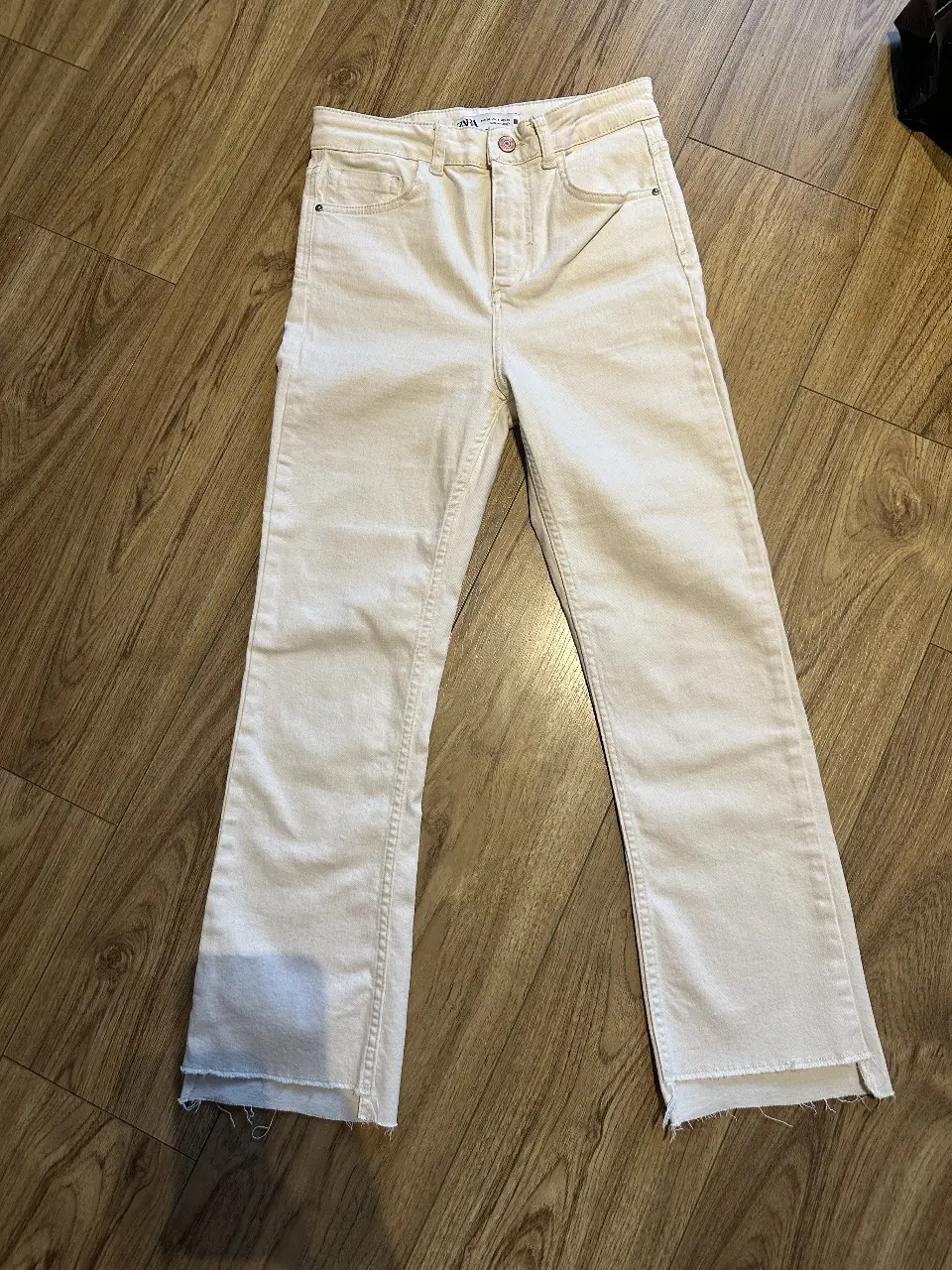 Jeans rectos color crudo de la marca Zara, tiro alto, con un corte en el bajo. Ideal para un look casual y moderno.