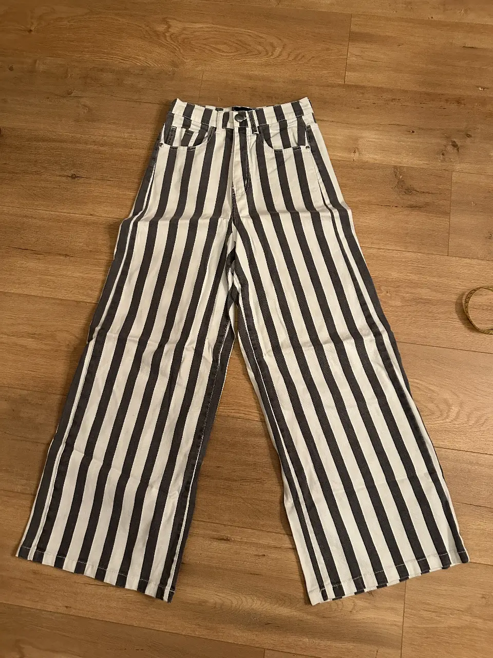 Pantalón de mujer a rayas verticales en blanco y negro. Tiro alto, corte ancho y bolsillos delanteros. Ideal para un look casual y moderno.