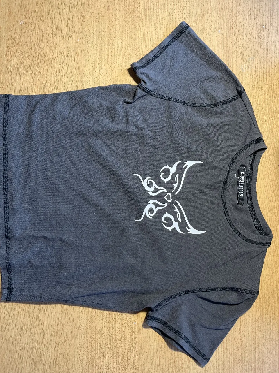 Remera manga corta gris oscuro con estampa de mariposa tribal blanca en el frente. Diseño con costuras al tono y corte moderno. Ideal para un look casual y canchero.