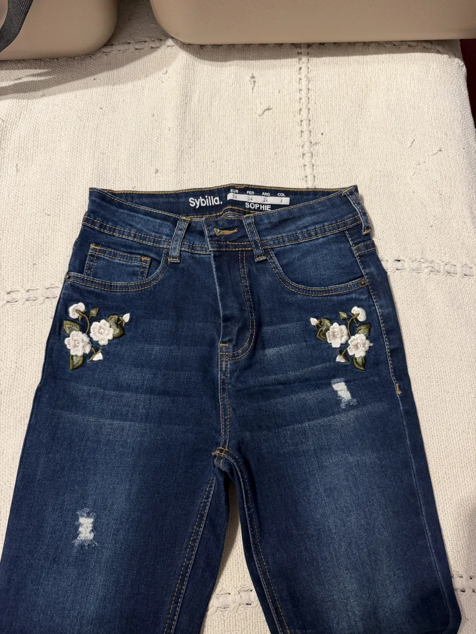 Jean de tiro alto con bordados florales en los bolsillos delanteros y detalles de roturas. Un diseño único y canchero para lucir en cualquier ocasión.