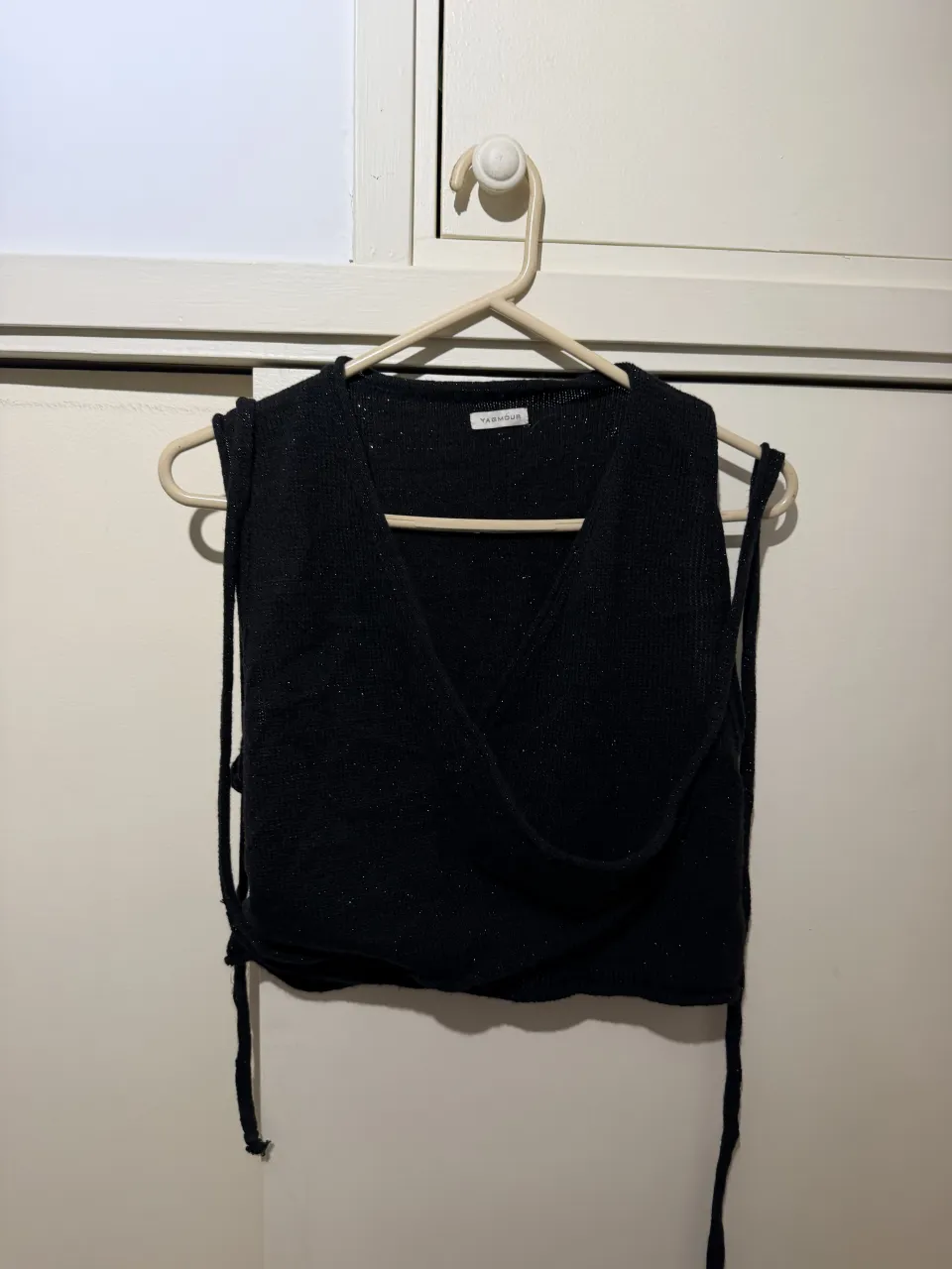 Top negro de tejido con brillos, escote cruzado y tiras para atar. Ideal para un look canchero y moderno.