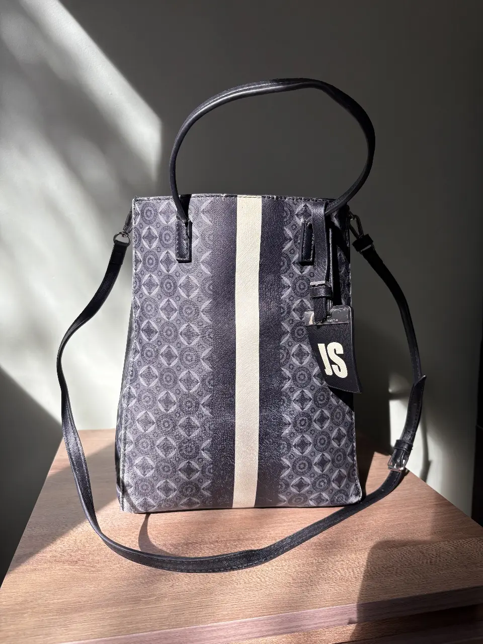 Bolso tote negro con diseño geométrico y detalles en blanco. Ideal para llevar todo lo necesario con estilo. Cuenta con manijas cortas y correa larga ajustable. cuenta con algunos detalles del uso